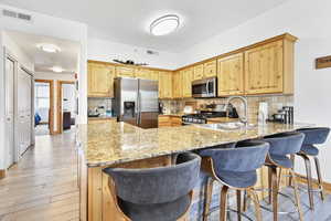 Kitchen featuring a sink, stainless steel appliances, visible vents, light stone counters, and a peninsula