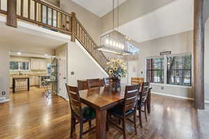 Dining room featuring stairs, baseboards, wood finished floors, and a towering ceiling