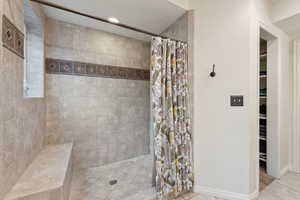 Full bath featuring baseboards, a walk in closet, tiled shower, and tile patterned floors