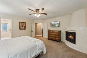 Bedroom featuring a ceiling fan, a large fireplace, baseboards, ensuite bathroom, and light carpet