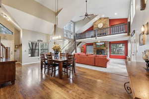 Dining area featuring a stone fireplace, a ceiling fan, high vaulted ceiling, and stairway