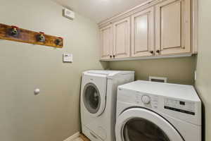 Laundry room featuring separate washer and dryer, cabinet space, and baseboards