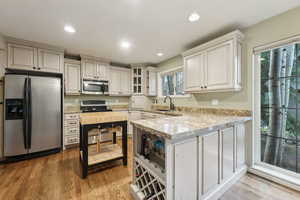 Kitchen with appliances with stainless steel finishes, wood finished floors, a sink, a peninsula, and glass insert cabinets