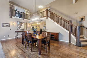 Dining space with stairway, baseboards, wood finished floors, and a towering ceiling