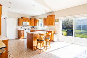 Kitchen featuring a breakfast bar, a sink, white appliances, light countertops, and a kitchen island