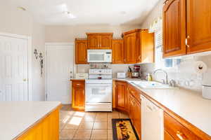 Kitchen with a sink, light countertops, brown cabinetry, and white appliances