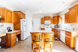 Kitchen featuring brown cabinets, a sink, white appliances, light countertops, and a center island