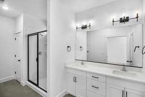 Full bathroom featuring baseboards, a sink, double vanity, and a shower stall