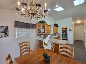 Dining room featuring baseboards, vaulted ceiling, dark carpet, and an inviting chandelier