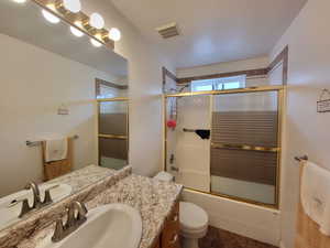 Full bath featuring vanity, toilet, shower / bath combination with glass door, and visible vents