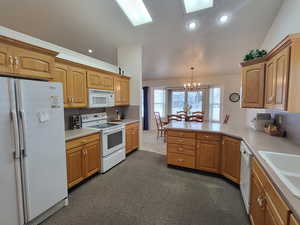 Kitchen featuring light countertops, a peninsula, a chandelier, white appliances, and dark carpet