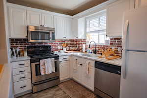 Kitchen with dark wood-style flooring, appliances with stainless steel finishes, a sink, light countertops, and white cabinetry