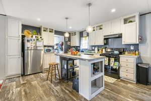 Kitchen with open shelves, gas stove, freestanding refrigerator, white microwave, and under cabinet range hood