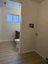 Half bath with visible vents, wood finished floors, vanity, baseboards, and toilet