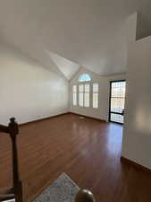 Unfurnished living room featuring baseboards, lofted ceiling, and wood finished floors