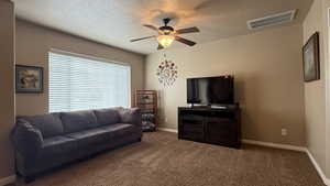 Carpeted living area with a textured ceiling, visible vents, ceiling fan, and baseboards