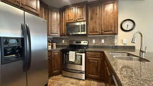 Kitchen featuring light tile patterned floors, a sink, backsplash, and stainless steel appliances