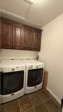 Clothes washing area featuring washing machine and dryer, cabinet space, baseboards