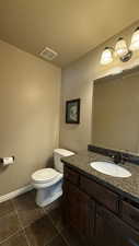 Half bathroom with vanity, toilet, visible vents, baseboards, and tile patterned flooring