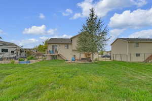 Rear view of house with a lawn, a wooden deck, a vegetable garden, stairway, and fence