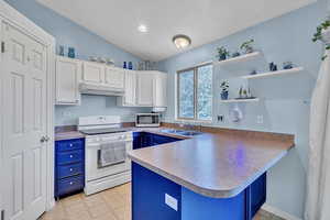 Kitchen with blue cabinets, a sink, a peninsula, white range with electric stovetop, and under cabinet range hood