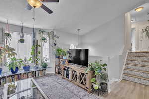 Living room featuring a textured ceiling, stairs, a ceiling fan, baseboards, and wood finished floors
