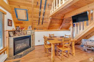 Dining area with wood ceiling, visible vents, a fireplace with flush hearth, wood finished floors, and vaulted ceiling with beams