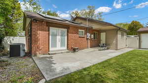 Rear view of property featuring french doors, solar panels, a gate, brick siding, and cooling unit