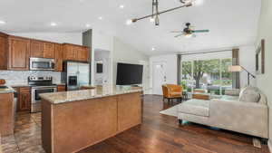 Kitchen with light stone countertops, open floor plan, ceiling fan, a center island, and appliances with stainless steel finishes