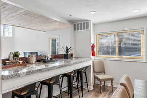 Kitchen with light stone countertops, visible vents, a breakfast bar, and wood finished floors