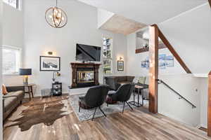 Living area with an inviting chandelier, high vaulted ceiling, a glass covered fireplace, baseboards, and wood finished floors