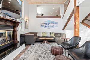 Living room featuring a high ceiling, a glass covered fireplace, dark wood-style floors, and wood ceiling