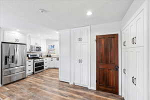 Kitchen featuring tasteful backsplash, appliances with stainless steel finishes, white cabinets, and wood finished floors