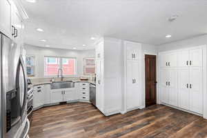 Kitchen with dark wood finished floors, appliances with stainless steel finishes, a sink, and light stone counters