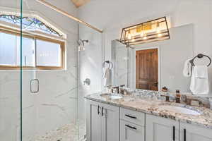 Bathroom with a sink, a marble finish shower, and double vanity