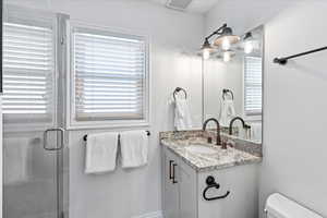 Full bath featuring vanity, toilet, visible vents, and a stall shower