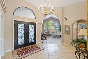 Entryway featuring light tile patterned floors, high vaulted ceiling, french doors, and a notable chandelier
