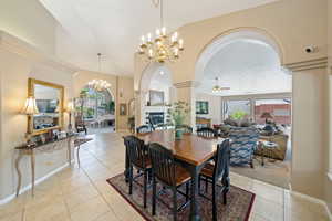 Dining space with ornate columns, a large fireplace, arched walkways, ceiling fan with notable chandelier, and light tile patterned floors