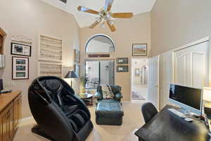 Home office with high vaulted ceiling, baseboards, a ceiling fan, and light colored carpet