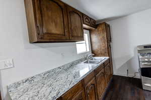 Kitchen featuring dark wood-style flooring, light stone counters, stainless steel gas range oven, a sink, and baseboards