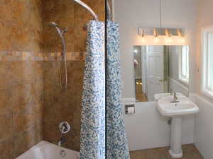 Full bathroom with a wainscoted wall, a sink, and shower / bathtub combination with curtain in White Door unit 2.