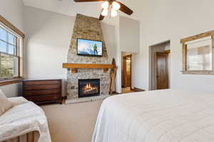 Carpeted bedroom with a stone fireplace, a ceiling fan, and high vaulted ceiling