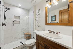 Full bath with toilet, a marble finish shower, and vanity