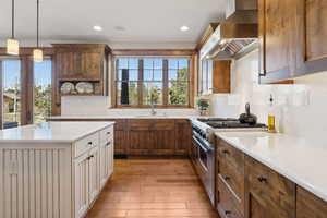 Kitchen with wall chimney range hood, stainless steel range, a sink, light countertops, and light wood-style flooring
