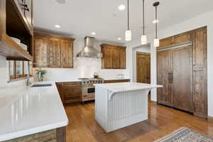 Kitchen featuring wall chimney range hood, brown cabinetry, designer stove, and a sink