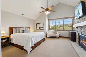 Bedroom with light carpet, high vaulted ceiling, a stone fireplace, a ceiling fan, and visible vents