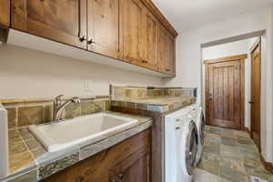 Laundry area with a sink, cabinet space, independent washer and dryer, and stone finish flooring