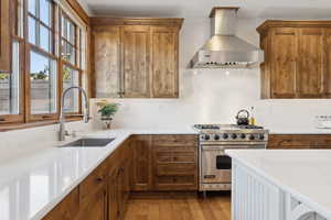 Kitchen with brown cabinets, wood finished floors, a sink, premium range, and wall chimney exhaust hood