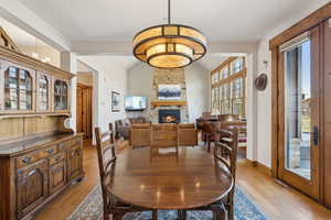 Dining space with baseboards, a fireplace, vaulted ceiling, and light wood finished floors