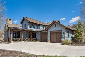 View of front of house with stone siding, a garage, a chimney, covered porch, and driveway